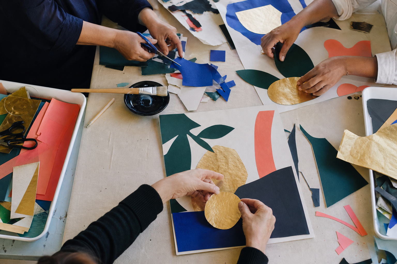 Handen rangschikken groene, gouden, blauwe en koraalkleurige papiervormen op een werktafel